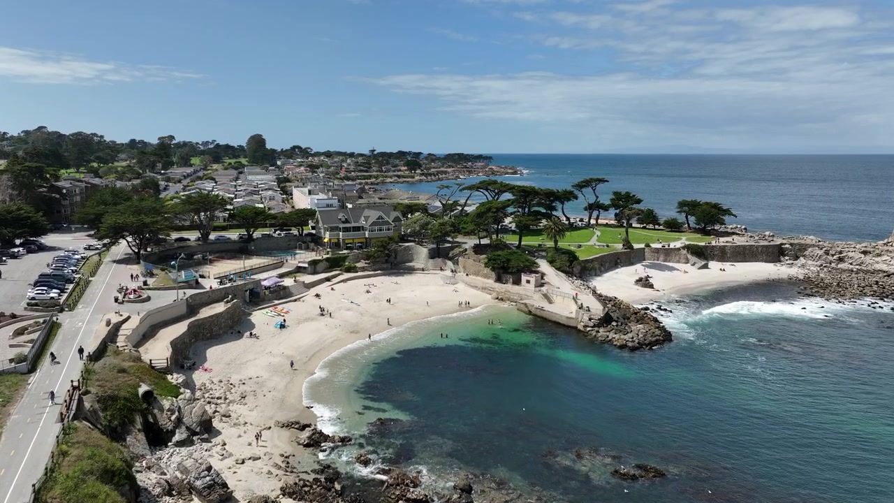 Riprese aeree cinematografiche con drone di Lovers Point Park a Pacific Grove, California, che mostrano la costa rocciosa, l'acqua turchese dell'oceano, una caletta sabbiosa, una strada costiera panoramica, case fronte mare, Monterey.