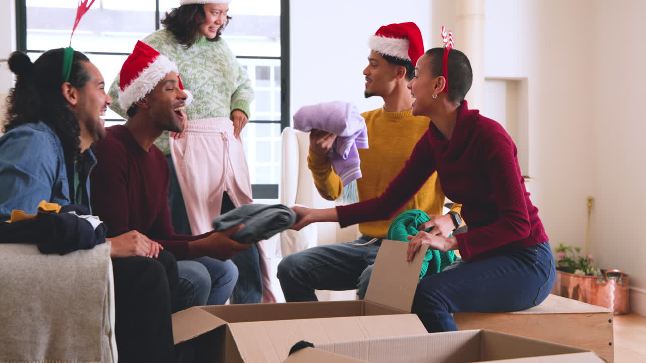 At christmas, young diverse friends wearing festive hats packing clothes for donations at home