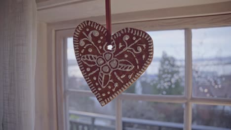 red gingerbread heart hanging in a window, snow-covered trees in background