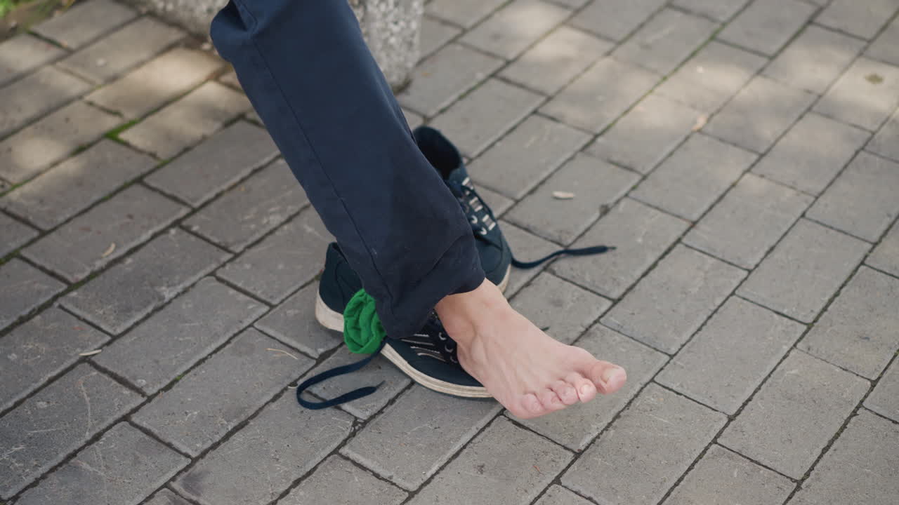 Barefoot in city, Removing footwear during urban outdoor stroll, Relaxedly taking off shoes amidst city surroundings, Enjoying freedom of barefoot walking in bustling modern environment
