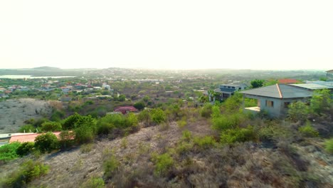 Vuelo-Cinematográfico-De-4k-Por-Una-Colina-Cubierta-De-Vegetación,-Hacia-La-Puesta-De-Sol-Que-Revela-Impresionantes-Casas-En-Barrios-De-La-Isla-Caribeña-De-Curacao