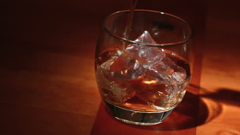 tumbler of ice being filled with whiskey