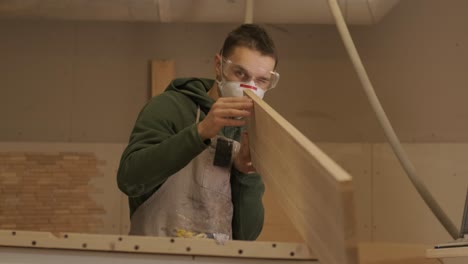 woodworker professional in mask and glasses checks wood raw, wooden plank, plywood panel