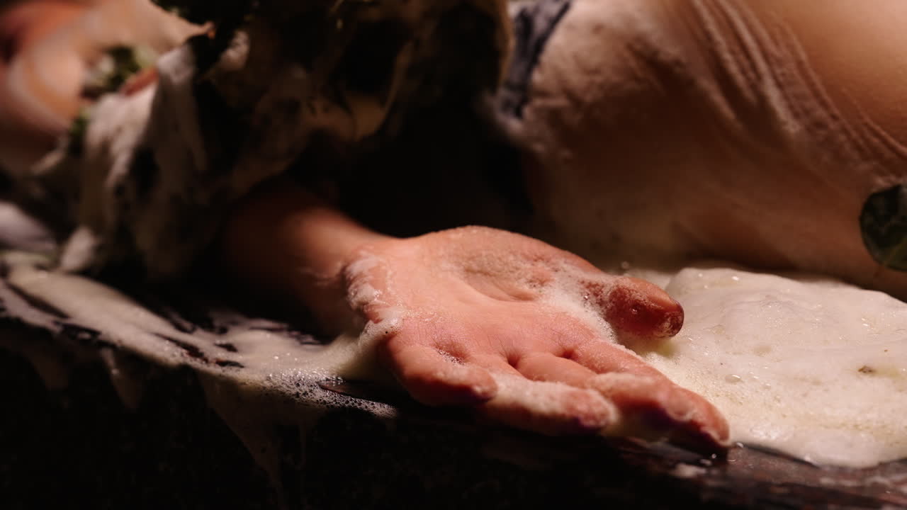 Woman washing body with soap and leaves in a bath