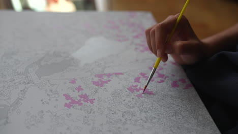 child painting with pink paintbrush on coloring book