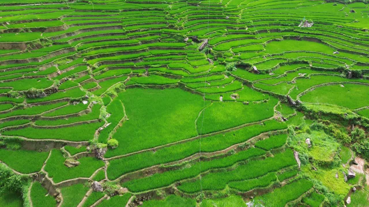 Aerial view of rice terraces and small village in Sapa, Vietnam, showing traditional houses, farmland, and dramatic mountain landscape