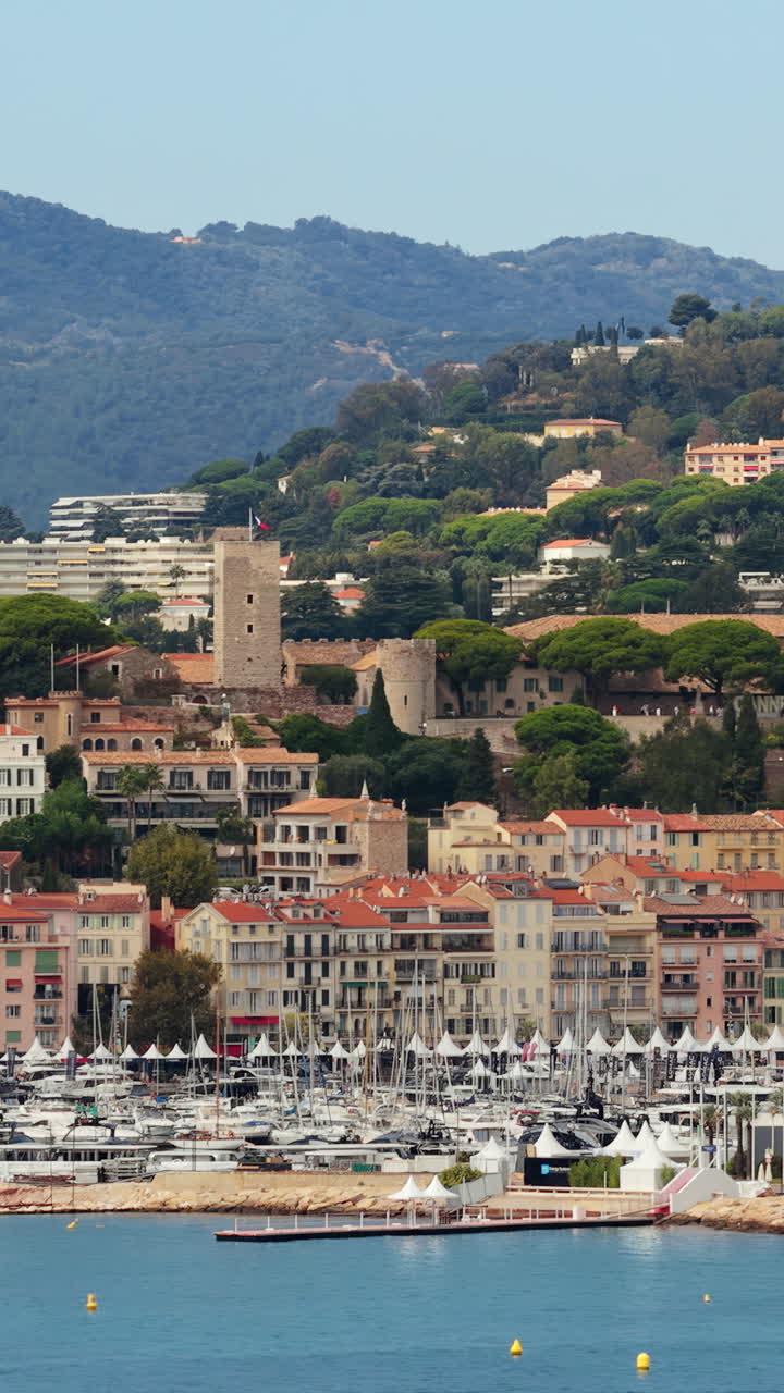 Aerial drone view of Cannes Old Town Le Suquet with historic tower, colorful rooftops, and luxury yachts in the marina. Vertical
