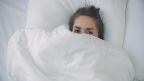 Mujer-Mirando-Debajo-Del-Edredón-Y-Sonriendo.-Una-Mujer-Alegre-Y-Sonriente-Asomándose-Por-Debajo-De-La-Manta-En-La-Cama-En-Casa-Y-Besando-La-Cámara