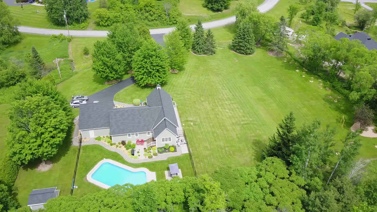 Rekaman drone 4K 360 derajat properti indah di musim panas di pedesaan Ontario, Kanada. Halaman rumput sempurna, kolam renang bersih, dedaunan hijau, halaman belakang luas, bungalo