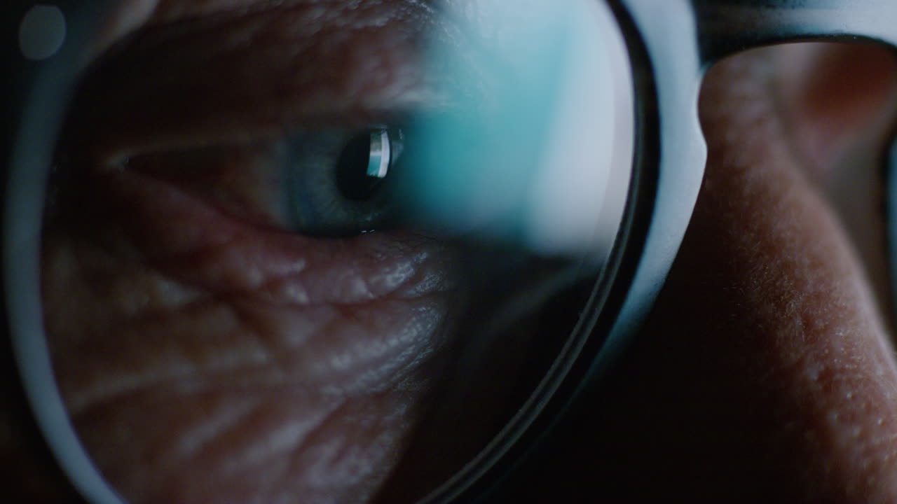 pantalla de ojo macro de cerca que se refleja en las gafas anciana navegando en línea por la noche