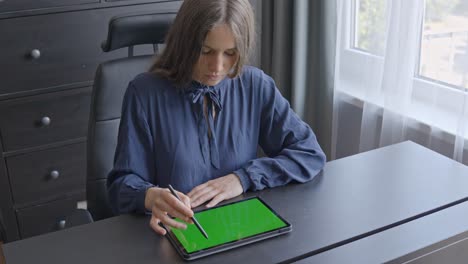 focused business woman working on her office table with green screen tablet