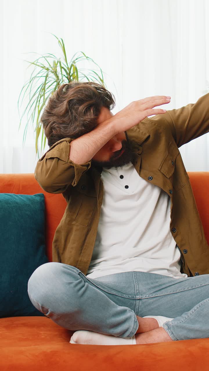 Happy man having fun dancing dabbing raising hands making dub dance gesture at home room on sofa