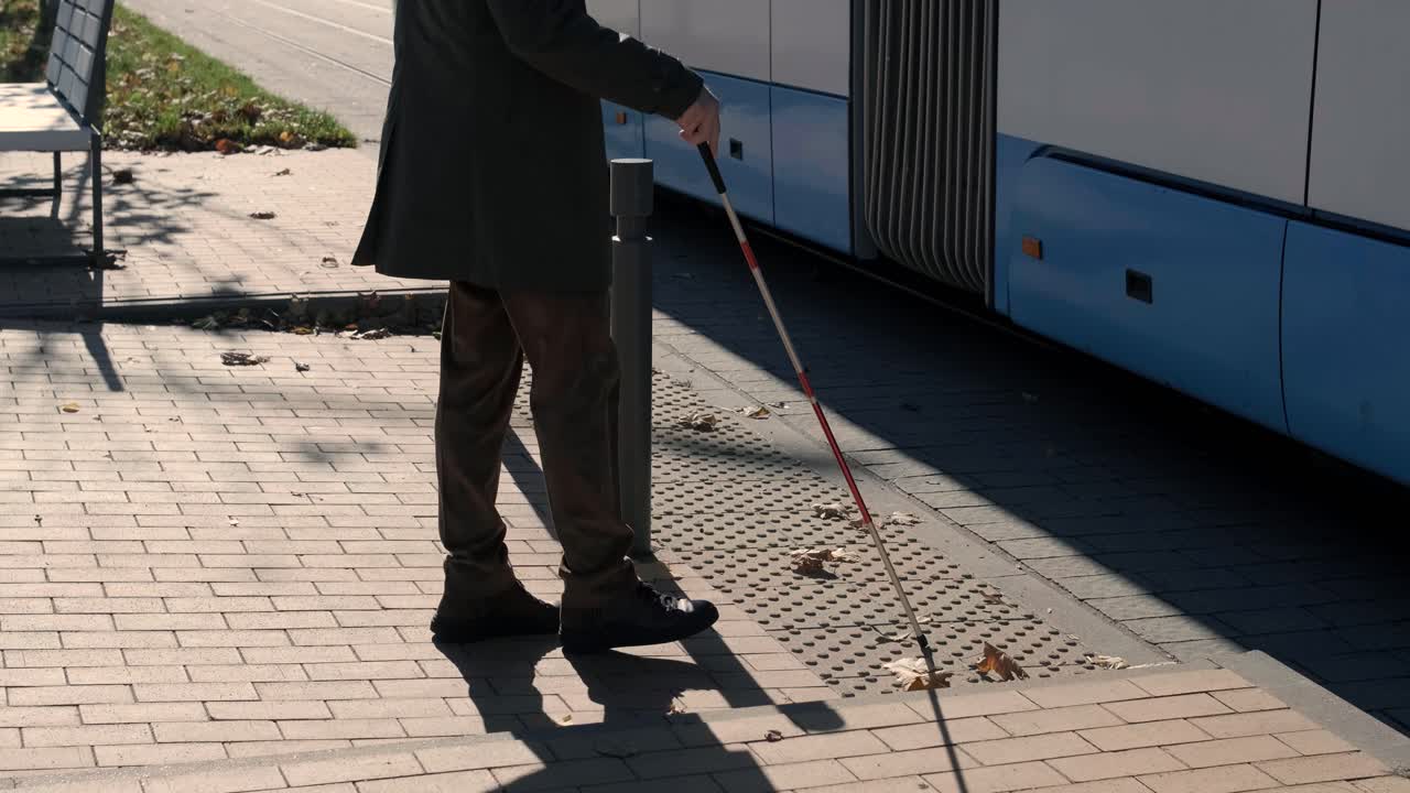 Visually impaired man crossing the road with his stick with the help of tactile pedestrian sidewalk for the visually impaired in the city.