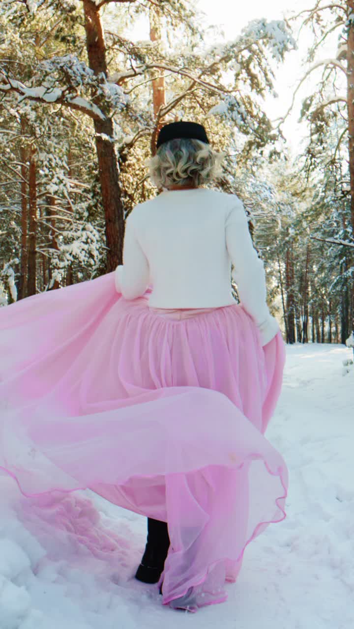 Donna elegante in abito rosa che volteggia in una foresta invernale innevata