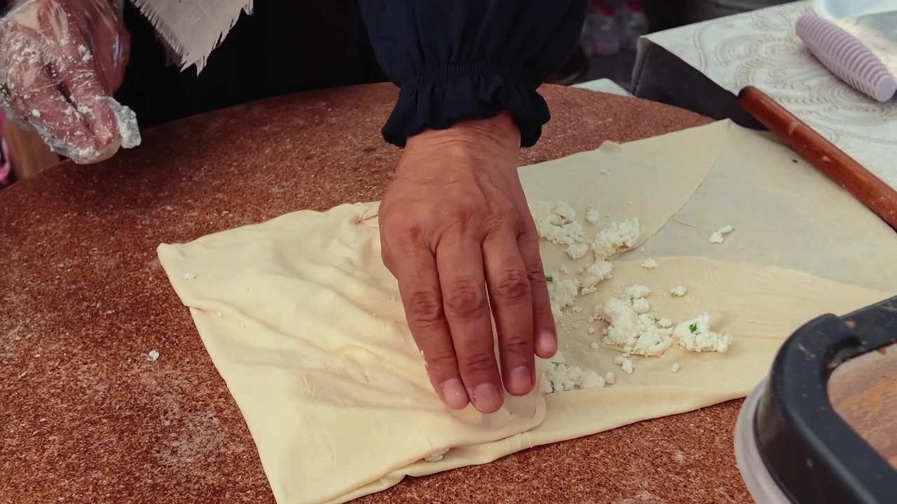 Persona preparando gozleme turco tradicional con relleno de queso.