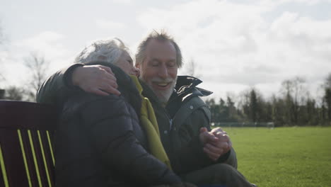 loving senior couple sitting on seat enjoying autumn or winter walk through park together