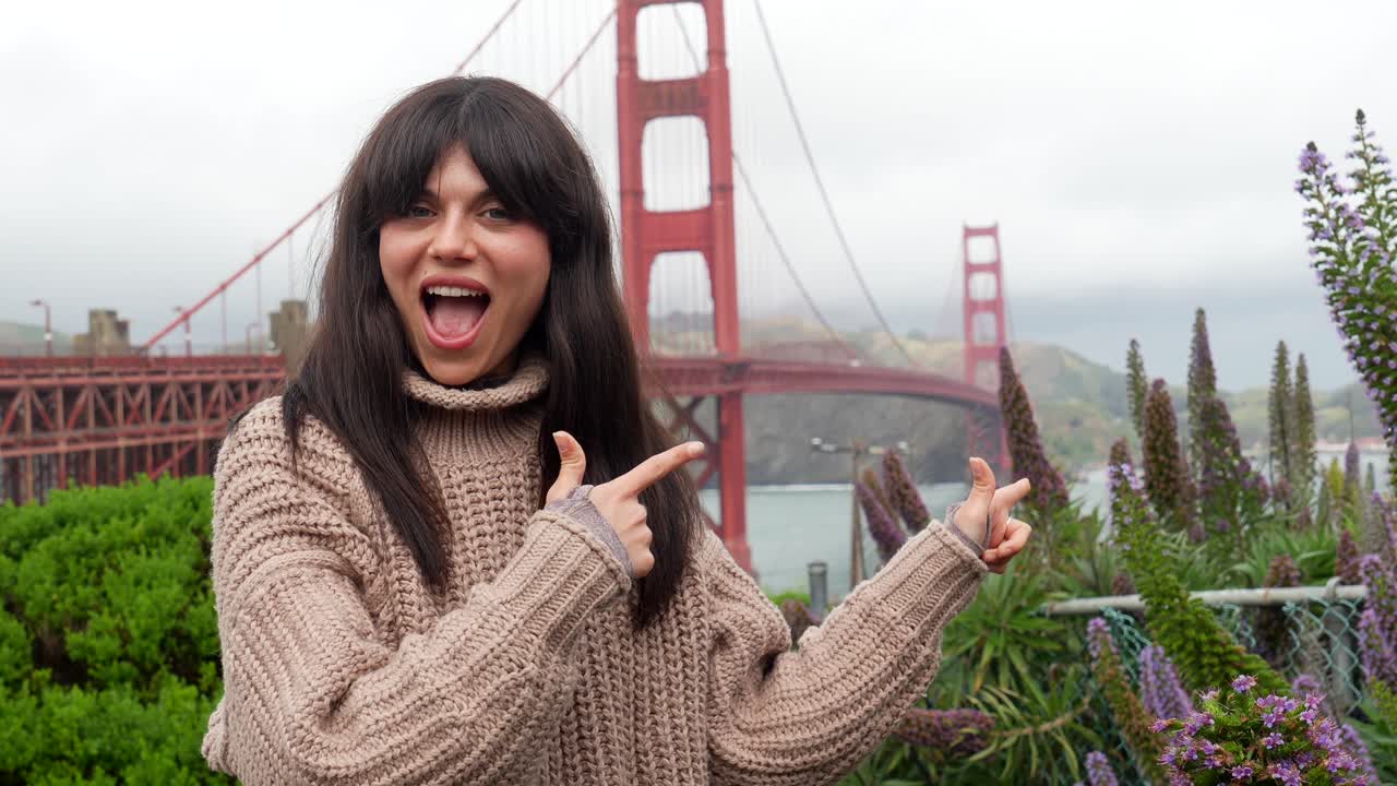 Wanita Muda Tersenyum dan Menunjuk dengan Jembatan Golden Gate di Latar Belakang