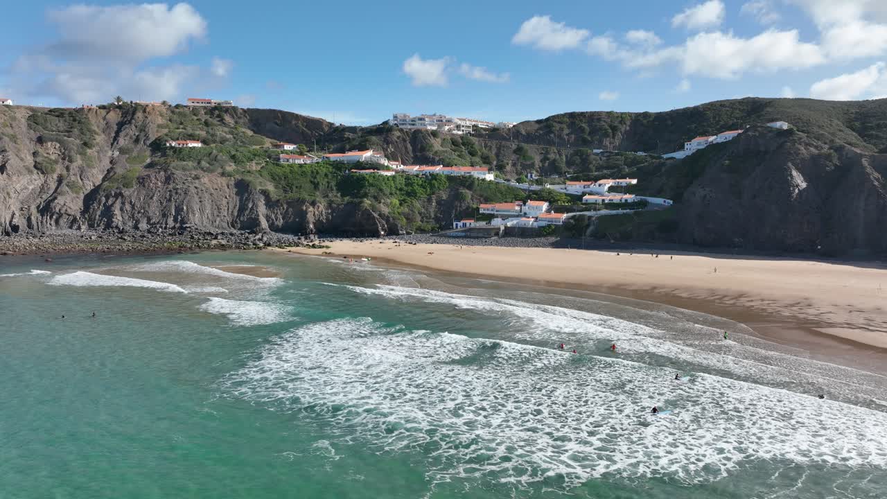 Scatto aereo di surfisti che cavalcano le onde su una bellissima spiaggia soleggiata circondata da scogliere
