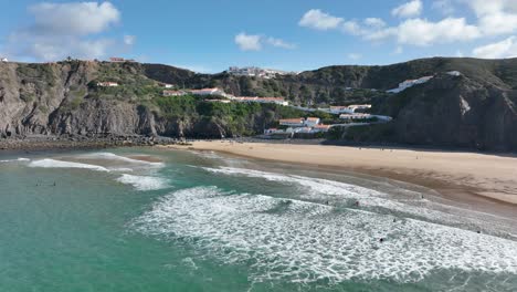 Toma-Aérea-De-Surfistas-Atrapando-Olas-En-Una-Hermosa-Playa-Soleada-Rodeada-De-Acantilados