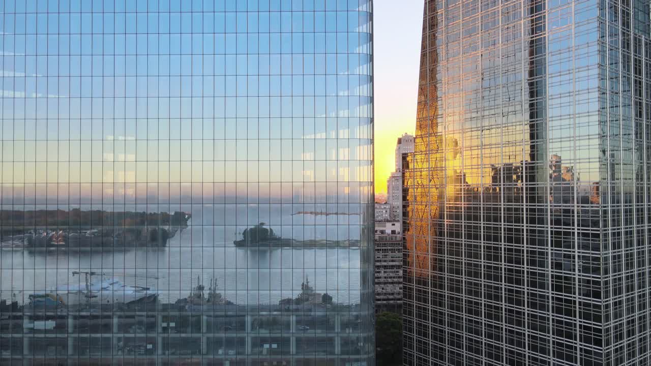 Arranha-céus de vidro da cidade de Buenos Aires com drone subindo em close-up dos edifícios, com o famoso porto de Puerto Madero perfeitamente refletido nas janelas de vidro durante a hora dourada do pôr do sol.