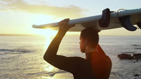 Vista-Trasera-De-Un-Surfista-Caucásico-De-Mediana-Edad-Llevando-Una-Tabla-De-Surf-En-La-Cabeza-En-La-Playa-4k