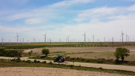 vista aérea de un tractor conduciendo por la carretera con molinos de viento en el fondo, en un día nublado y ventoso