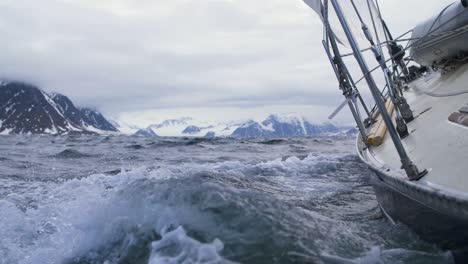 sailing a yacht in the high arctic seas in svalbard - slow motion shot waves crashing along hull