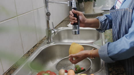 Young-African-American-woman-washes-vegetables-at-home,-with-copy-space