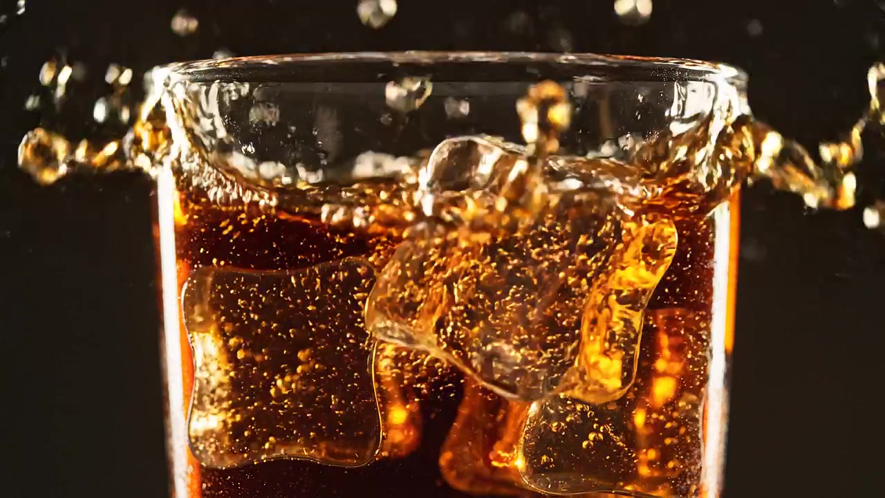 Schizzo di Cola con cubetti di ghiaccio in un bicchiere, primo piano