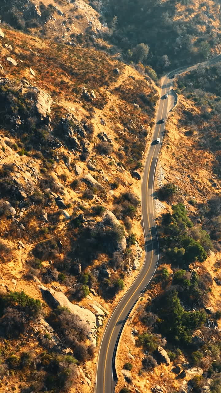 Four cars following each other by the highway in the mountains in California desert. Dangerous speedway over the mountainous river. Aerial view. Vertical video