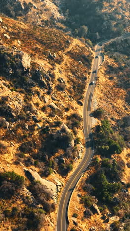 four cars following each other by the highway in the mountains in california desert. dangerous speedway over the mountainous river. aerial view. vertical video
