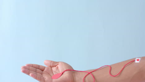 mano de hombre biracial con gota de sangre, cuerda roja y corazón pegando yeso en azul, cámara lenta
