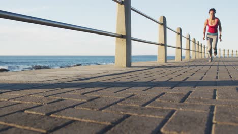 mujer afroamericana en ropa deportiva corriendo en el paseo marítimo por el mar