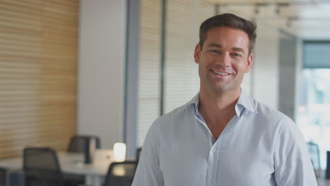 retrato de um empresário sorridente vestido casualmente de pé em um escritório moderno de plano aberto