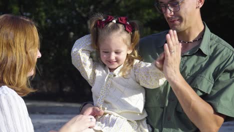 a happy young couple of parents are giving a high five to their daughter in a city park