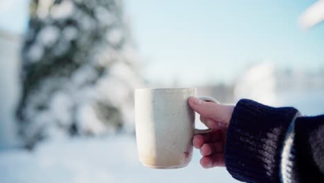 a man's hand grips a mug filled with a hot beverage on a winter day - close up