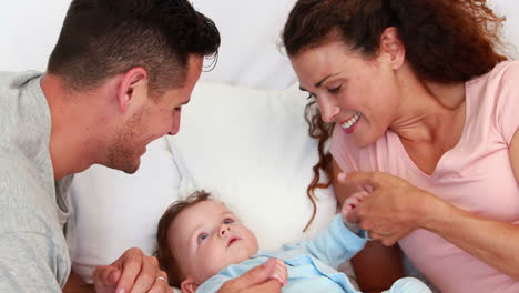 Baby-boy-in-blue-babygro-being-tickled-by-happy-parents-on-bed