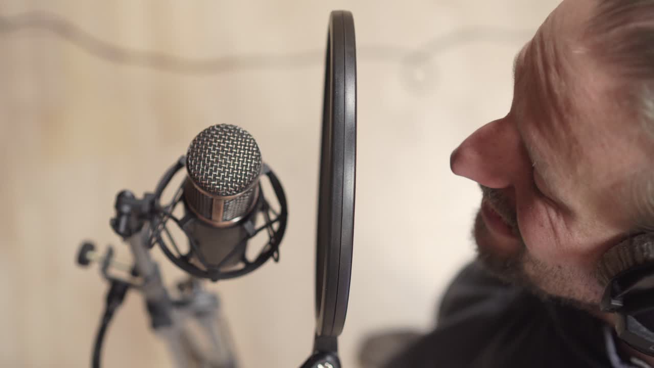 Male recording vocals on condenser microphone in sound studio, high angle perspective closeup view
