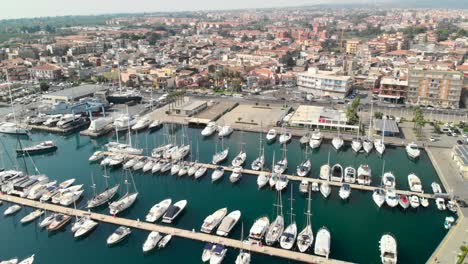 Aerial-tilt-down-reveal,-marina-full-of-boats-next-to-modern-mediterranean-town