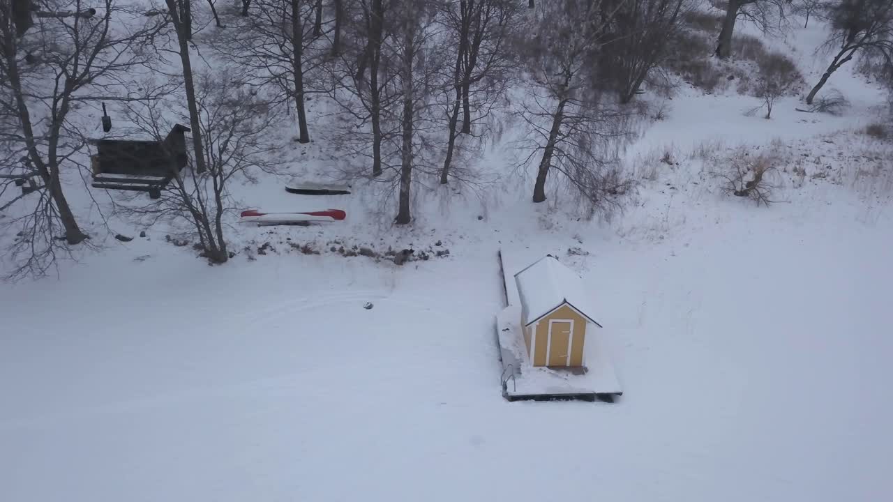 오른쪽에서 부드러운 패닝 샷은 숲 가장자리와 더 큰 소박한 오두막에서 불과 몇 걸음 떨어진 얼어붙은 호수 기슭에 있는 작은 오두막의 이상적인 위치를 보여줍니다.