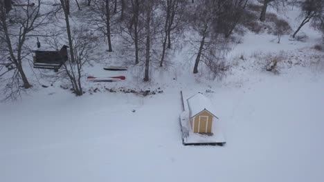 Smooth-panning-shot-from-right-hand-side-showing-ideal-location-of-tiny-cabin-on-the-shore-of-frozen-lake-only-few-steps-away-from-forest's-edge-and-bigger-rustic-cabin.