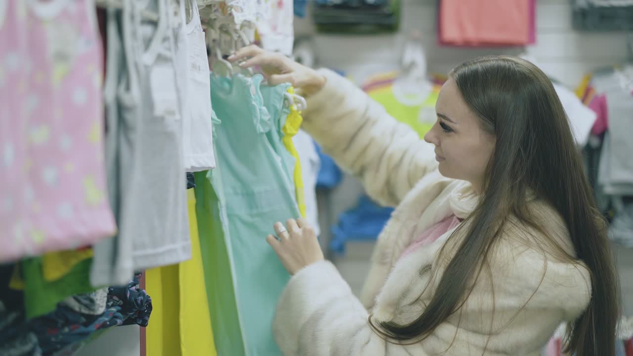 morena de pelo largo con abrigo de piel mira la ropa de los niños
