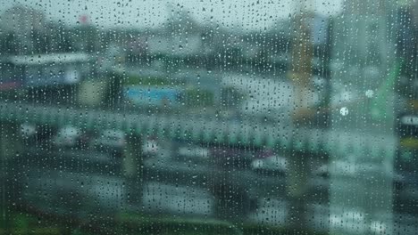 rain water drops falling down on the window glass , rain drops on the windows glass, close shot of water droplets falling .  a blouse car traffic in the background on a rainy and sad pandemic day.