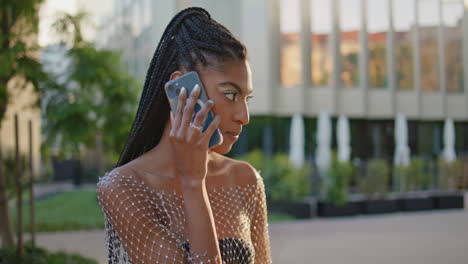 talking fashionista using mobile phone on city street in summer morning closeup