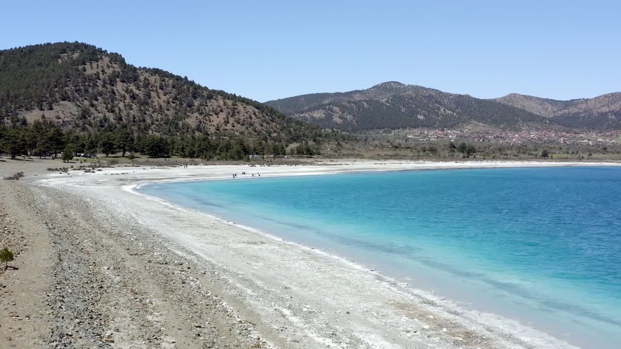 Descending drone to hills over white beach and turquoise water of Lake Salda