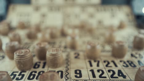 video macro de un tablero de bingo, luces de estudio, 120 fps, cámara lenta, dígitos de chips de madera, imágenes en bruto, juego de mesa de lotería, números de cartas, grúa zoom out movimiento suave