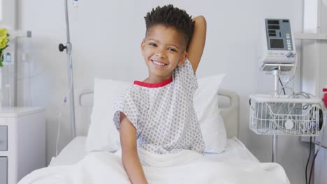 portrait of happy african american boy patient sitting up in bed at hospital smiling