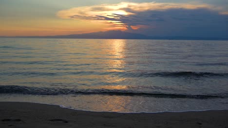 waves slowly splashing on a sandy beach while the sun is setting in the background behind a mountain peak, thassos island, greece