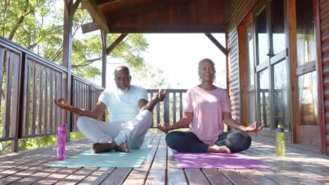 focused senior african american couple practicing yoga meditation on sunny terrace, slow motion