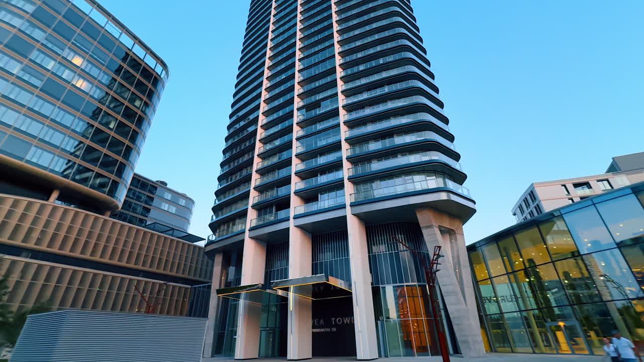 Urban modern architecture. Buildings with glass facades surround a green space, illuminated by evening light in a bustling city area
